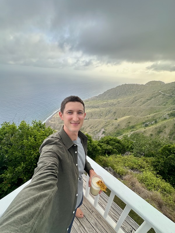 travel bloggerman holding a cocktail overlooking the rolling hills and valleys in Saba