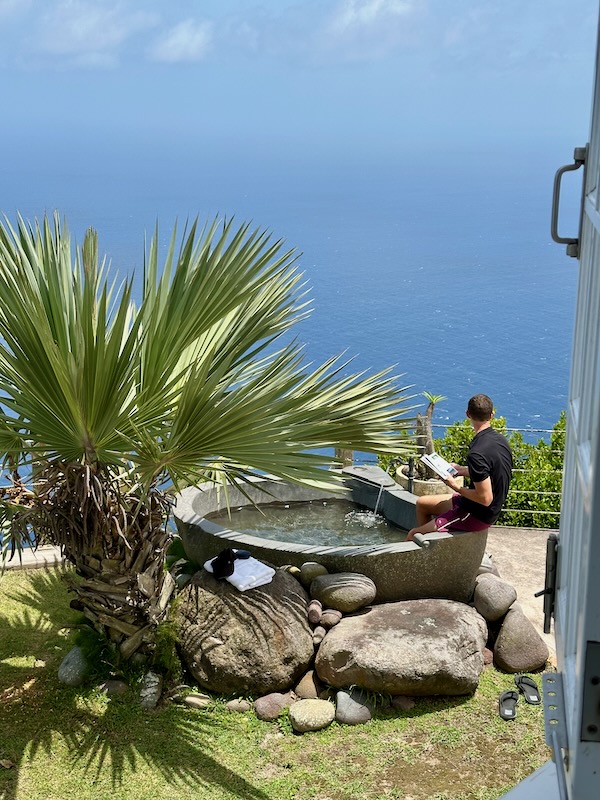 man sits in outdoor tub reading book overlooking Caribbean Sea from Spyglass villa in Saba 